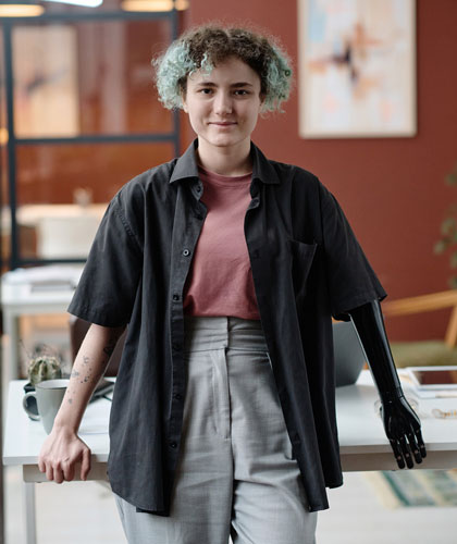 Persona con camisa negra y cabello rizado apoyada en una mesa, con una prótesis en el brazo derecho